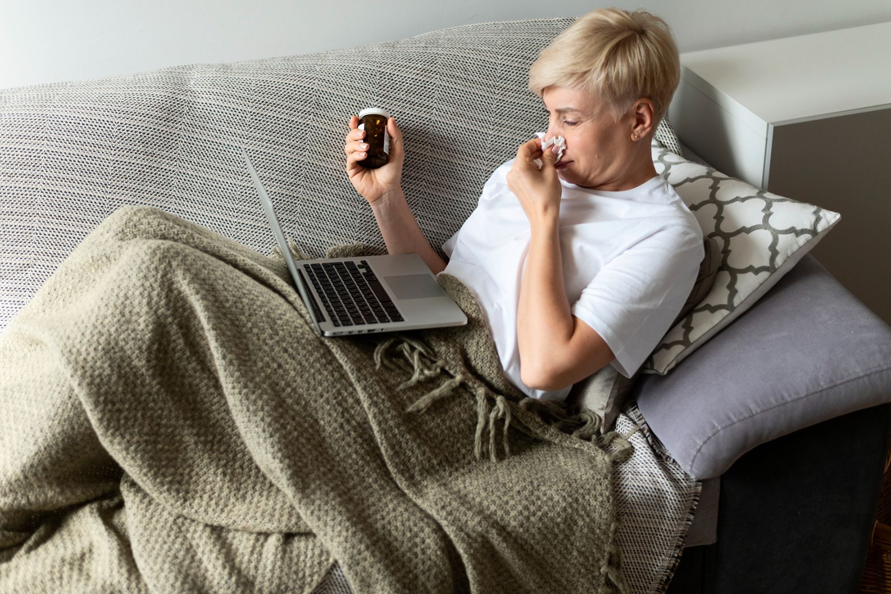 больная женщина лежит на диване с ноутбуком